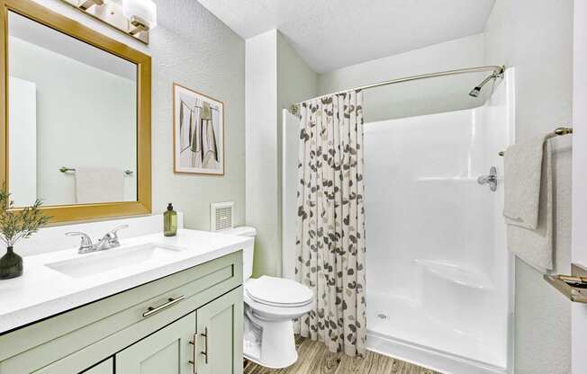 A bathroom with a white toilet, a sink with a green vase, a mirror, a shower with a curtain, and a towel.