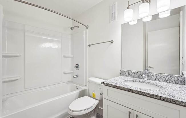 A bathroom with granite countertop, a toilet, sink, and shower.