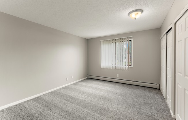 A room with a carpeted floor and a window with blinds.