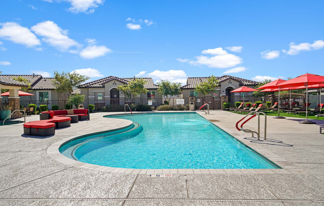 a swimming pool with red chairs and umbrellas and apartments in the background