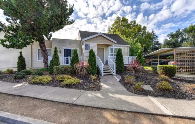 Apartment entrance with small staircase leading up to the front of the building and nice shrubs and tress outside of the building. 