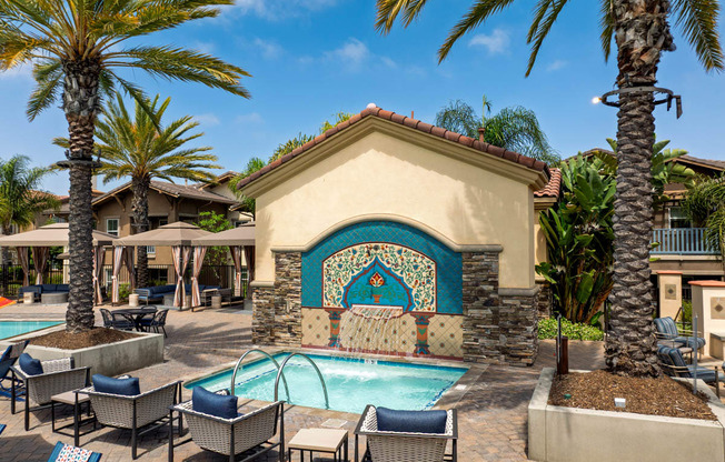 A pool area with a mosaic tile wall and lounge chairs.