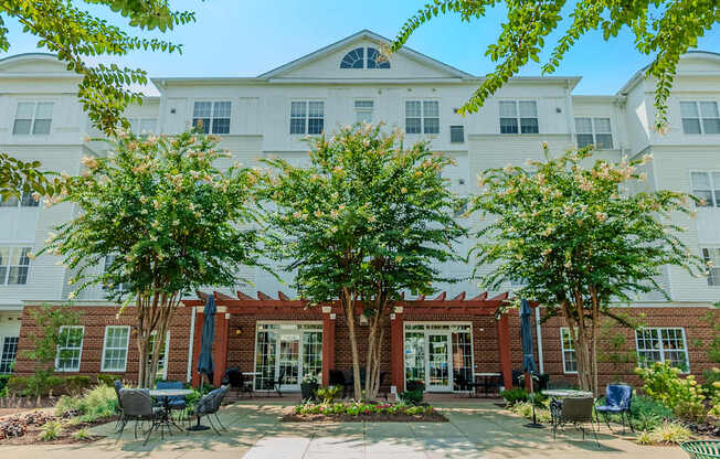 A white building with a red brick entrance and trees in front.