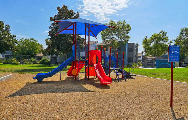 a playground with a blue umbrella and red slides