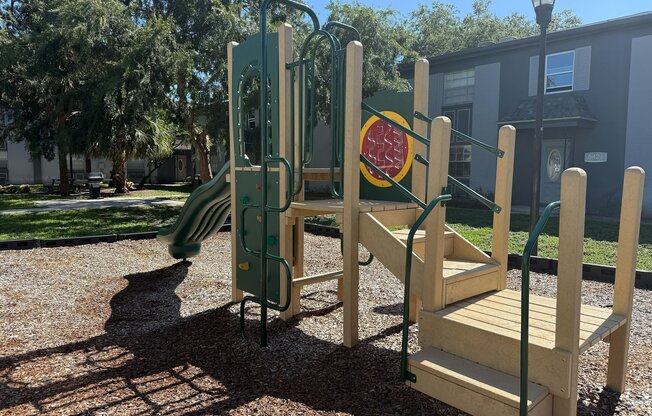 Inviting playground with a slide and climbing structure surrounded by lush greenery, perfect for family fun in a tranquil apartment community.
