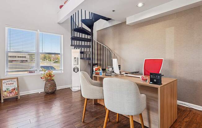 A room with a desk, chairs and a staircase.