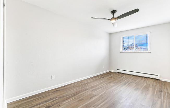 Bright empty room with elegant wooden flooring, large window with soothing views, and modern ceiling fan, offering a refreshing and versatile space.