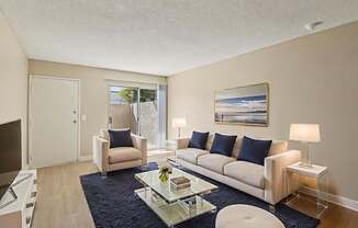 A living room with a white couch, a glass coffee table, and a painting on the wall.