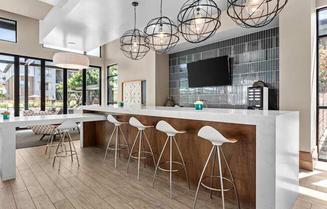 A modern kitchen with a bar area and white stools.
