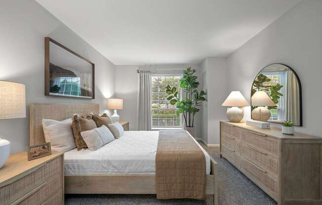 A well-lit bedroom with a large bed, a nightstand with a lamp, and a mirror on the wall.