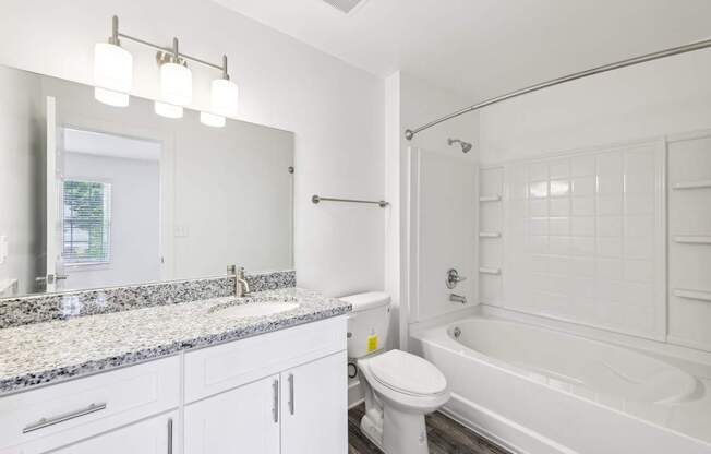 A white bathroom with a granite countertop and a white toilet.