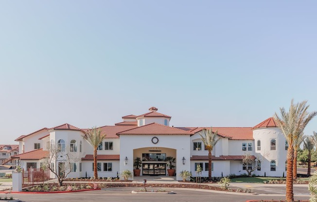 A large white building with a red roof and palm trees in front.