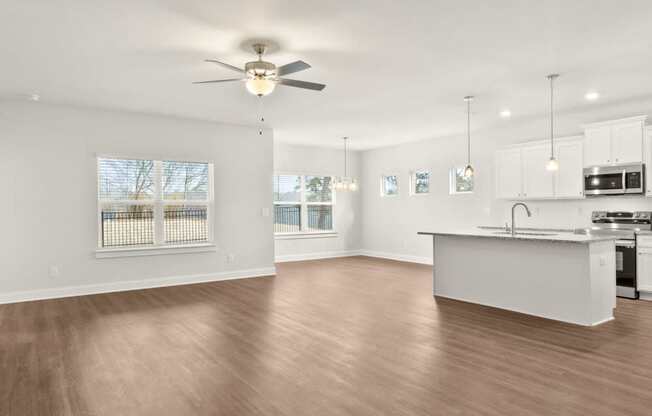 an empty living room with a kitchen and a ceiling fan