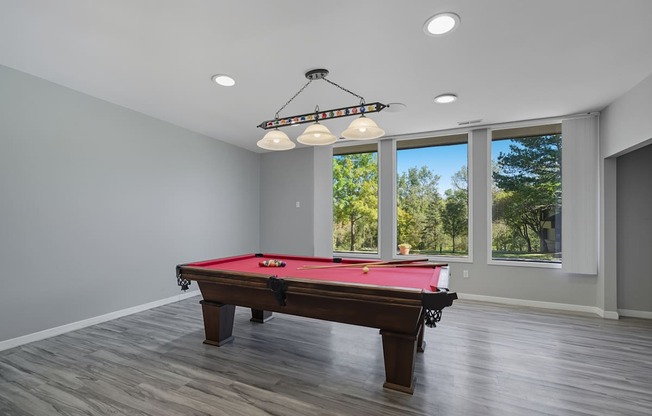 A pool table in a room with a view of trees outside the window.