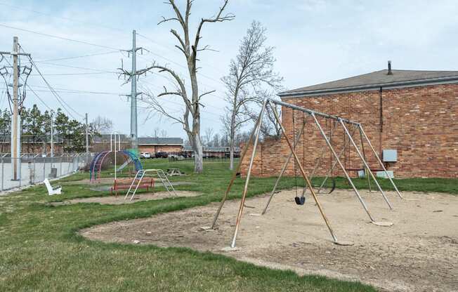 A playground with swings and a slide in front of a brick building.