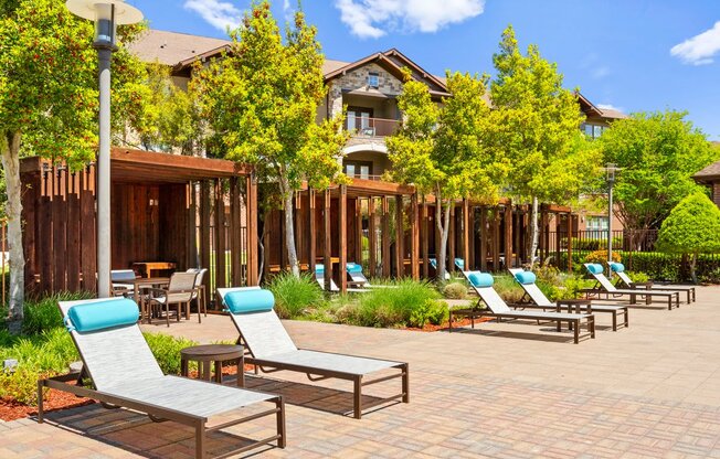 a patio with lounge chairs and tables and a building in the background