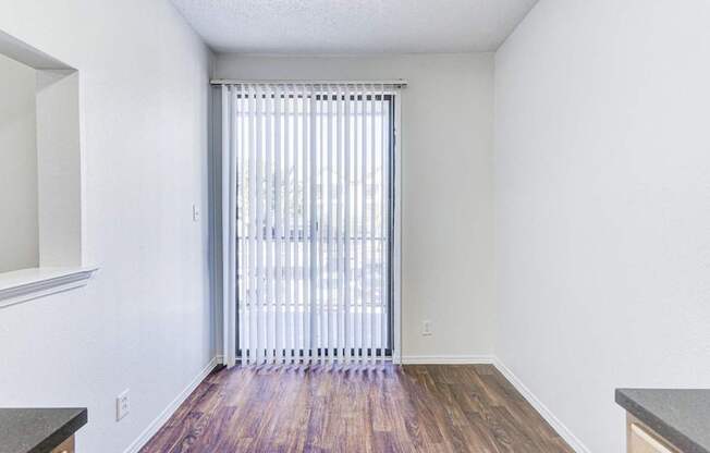 A dining area with wood-style flooring at Saxony at Chase Oaks Apartments in Dallas, TX, featuring a large sliding glass door with vertical blinds that opens to a balcony.