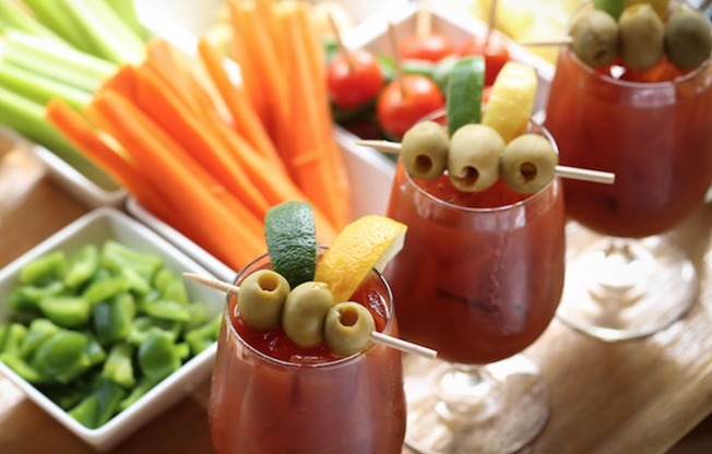 Three glasses of a red beverage with olives and lemon slices on top.