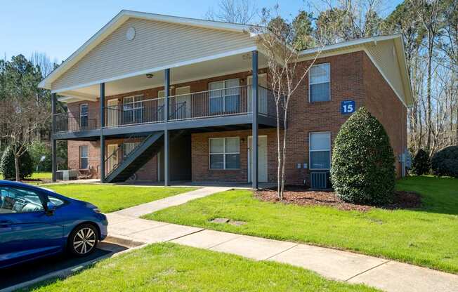 A blue car is parked in front of a two-story brick apartment building.