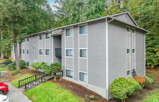 A grey apartment building with a red car parked in front.