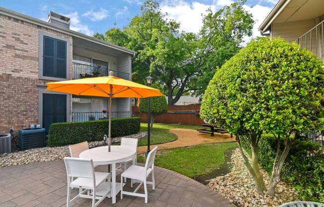 a patio with a white table with an orange umbrella and white chairs
