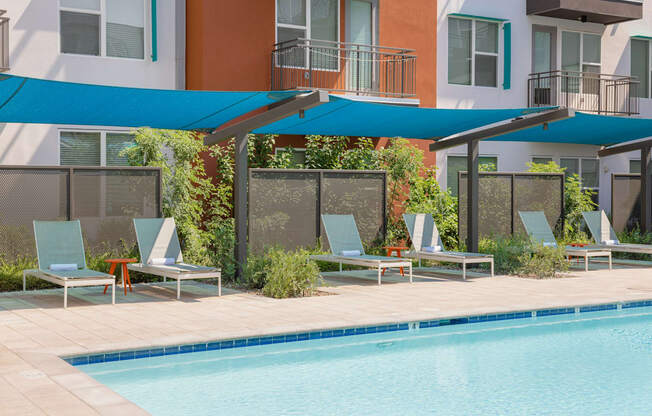 A pool with a blue canopy and lounge chairs.