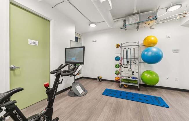 A room with a stationary bike, a TV monitor, and exercise equipment.