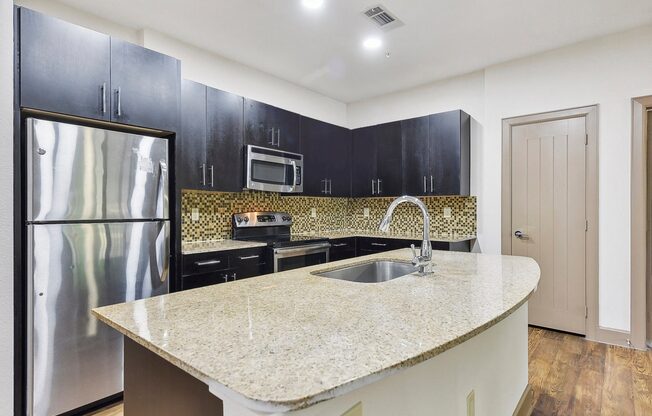 a kitchen with black cabinets and a granite counter top and a stainless steel refrigerator at Lakeline East Apartments, Cedar Park
