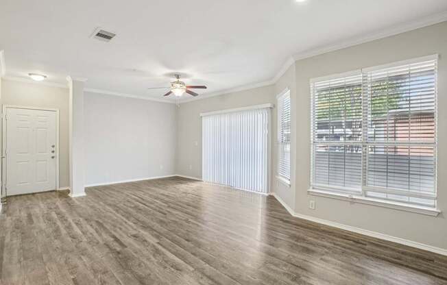 A room with a ceiling fan and two windows with blinds.