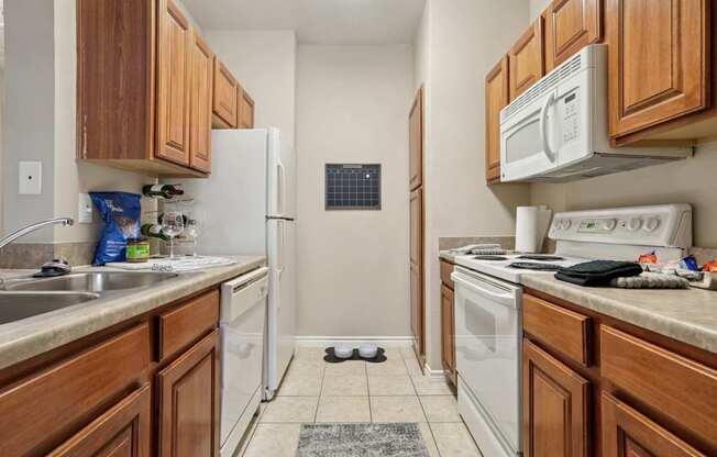 Windsor kitchen with wooden cabinets and white appliances at Encore at Buckingham Apartments in Richardson, TX