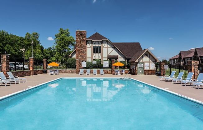A large swimming pool in front of a house with lounge chairs around it.