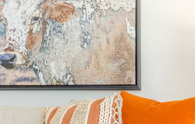 a white couch with an orange pillow and a painting of a cow