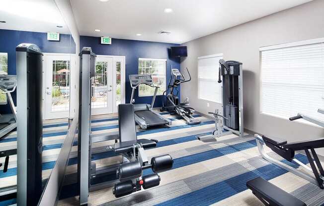 Ardenne Apartments fitness center with weight machines, treadmill, elyptical, blue and white carpet and blue accent wall