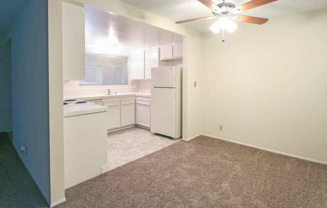 an empty kitchen with white appliances and a ceiling fan