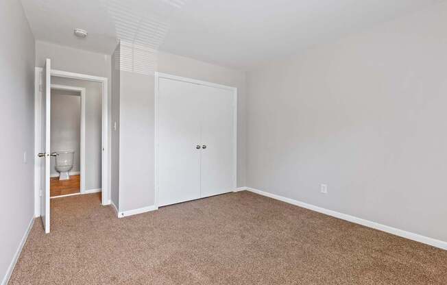 a bedroom with white walls and carpet and a door to a bathroom