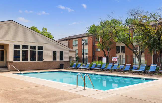 a swimming pool with blue chaise lounge chairs and a brick building in the background