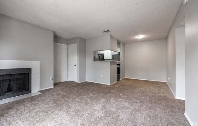 A spacious living room with a fireplace and a kitchenette in the background.