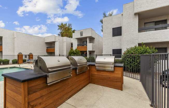 two bbq grills sit on a wooden deck in front of a pool