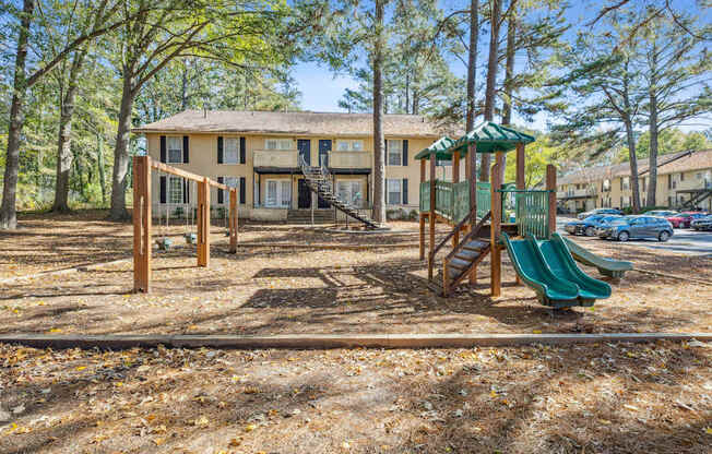 A playground with a green slide and a wooden swing set.
