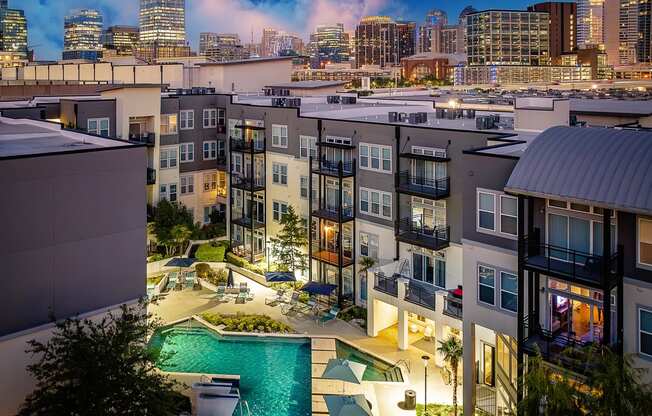 an aerial view of an apartment complex with a pool and cityscape in the background