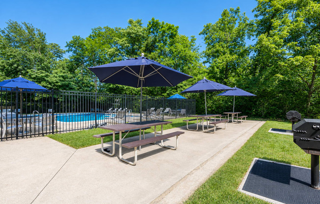 A sunny day at the poolside with picnic tables and umbrellas.