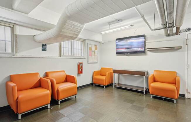 A room with orange chairs and a television mounted on the wall.