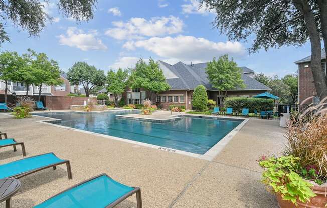A pool surrounded by lounge chairs and trees.
