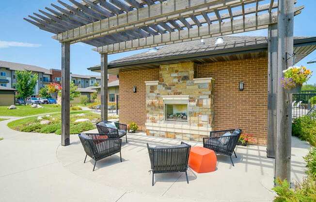 A patio with a stone fireplace and chairs under a pergola.