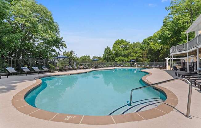 A large outdoor swimming pool surrounded by trees and lounge chairs.