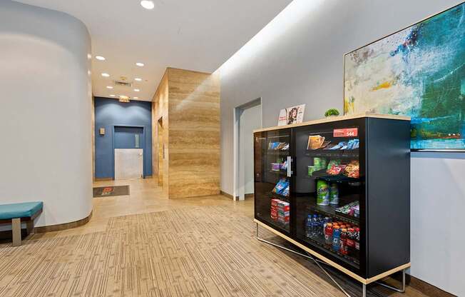 A modern office lobby with a bench, a vending machine, and a painting on the wall.