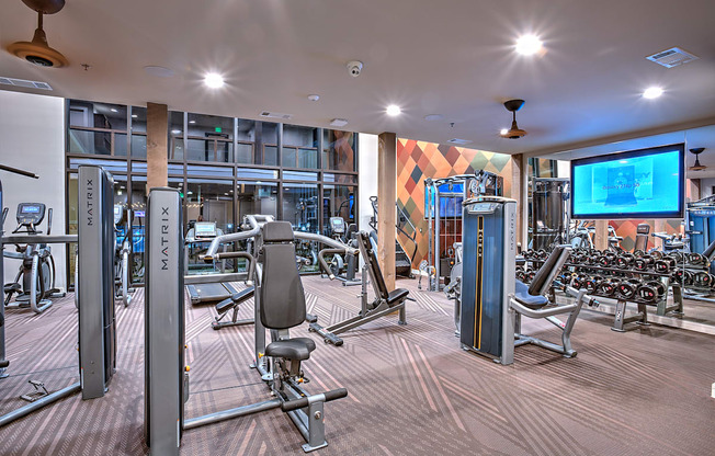 Gym with a variety of equipment including a squat rack, bench press, and a television at Edge and Stone, Texas, 78260