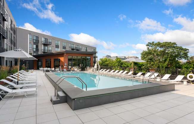 a swimming pool with chaise lounge chairs and umbrellas in front of a building