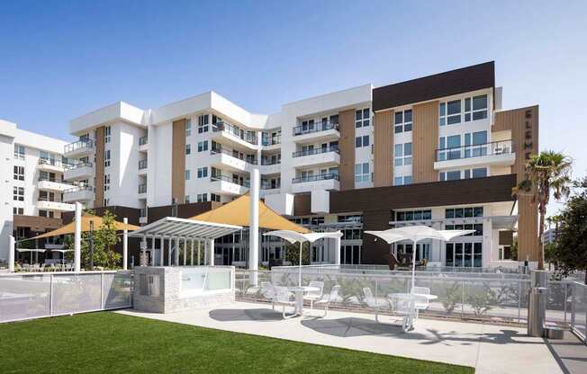 A modern building with a white fence and a grassy area in front. at Elements Apartments*, Irvine, California