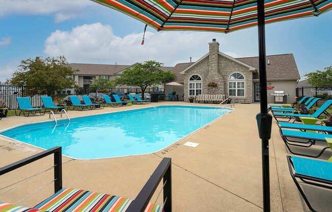 A pool with a striped umbrella and chairs.